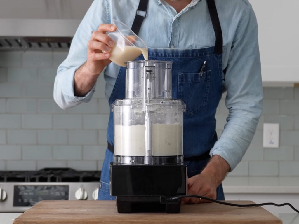 man adding liquid into food processor