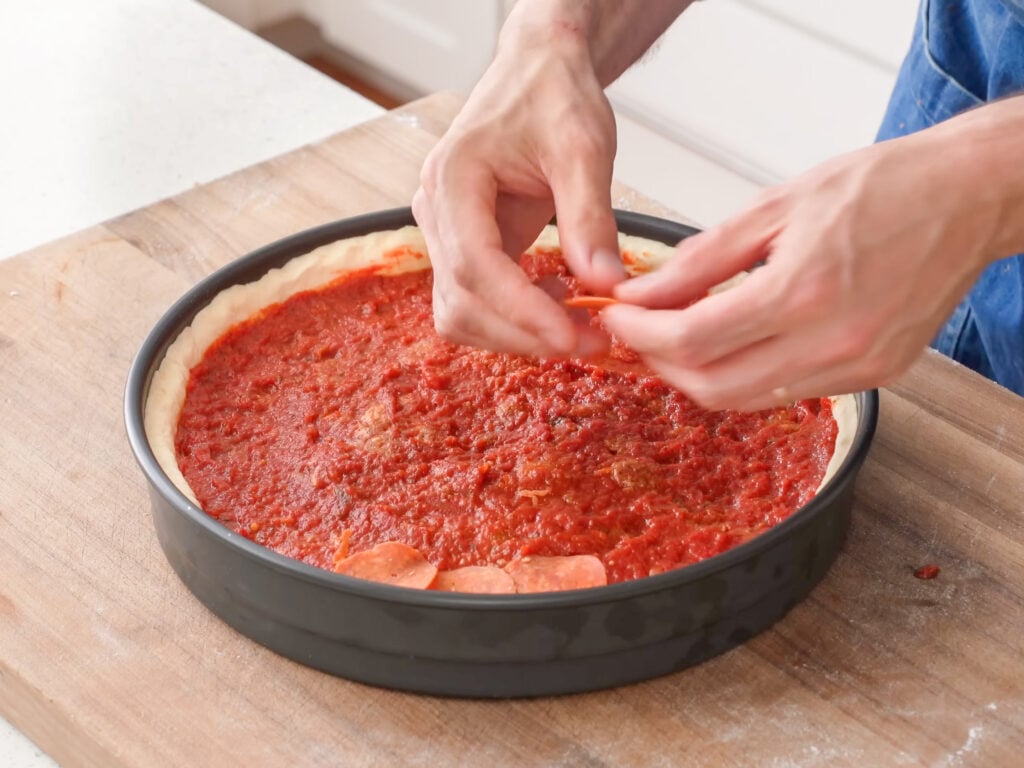 stacking pepperonis onto a sauced deep dish pizza