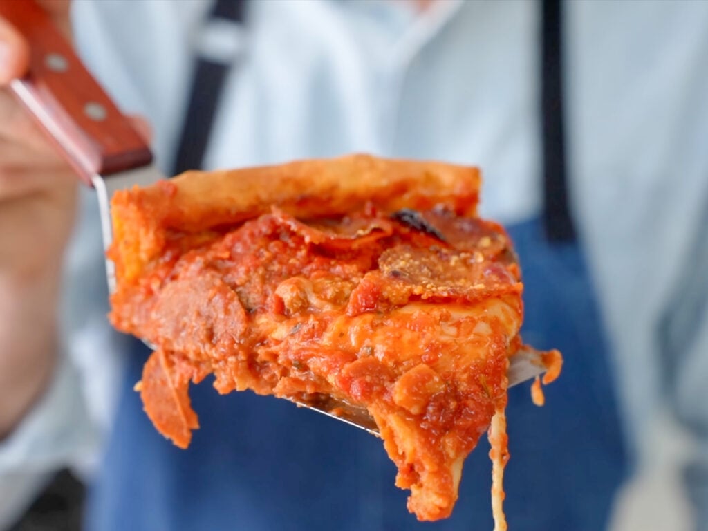 deep dish pizza slice being held toward camera