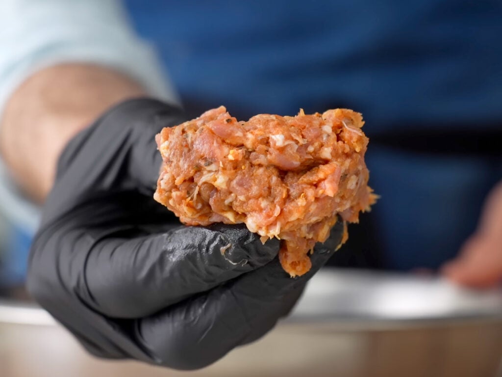 hand in black glove holding raw clump of Italian sausage
