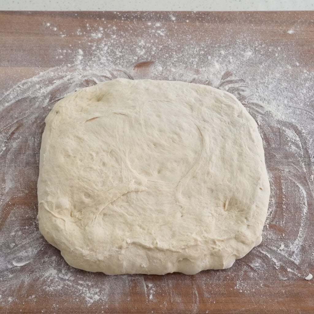 square of bread dough on floured wood cutting board 