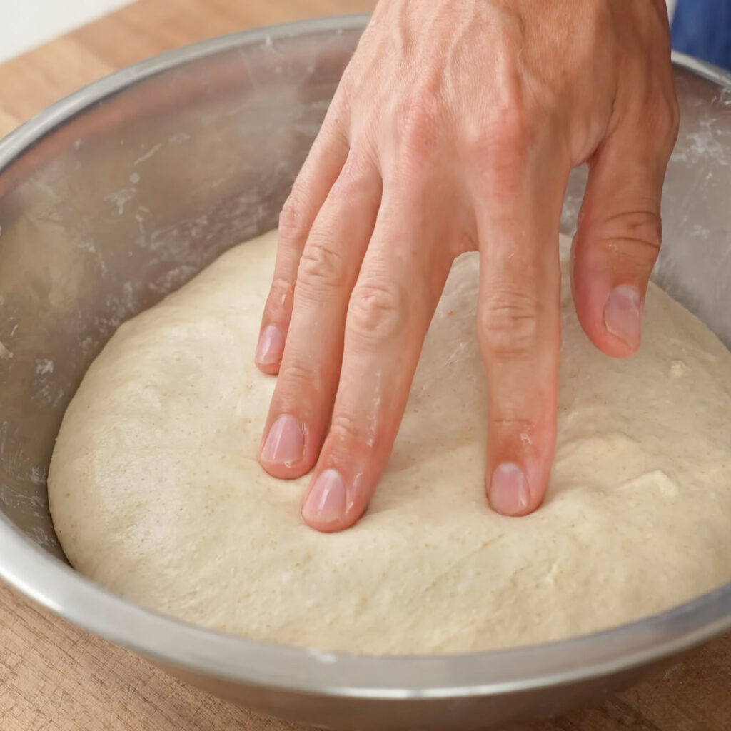 a hand poking ball of dough in metal bowl 