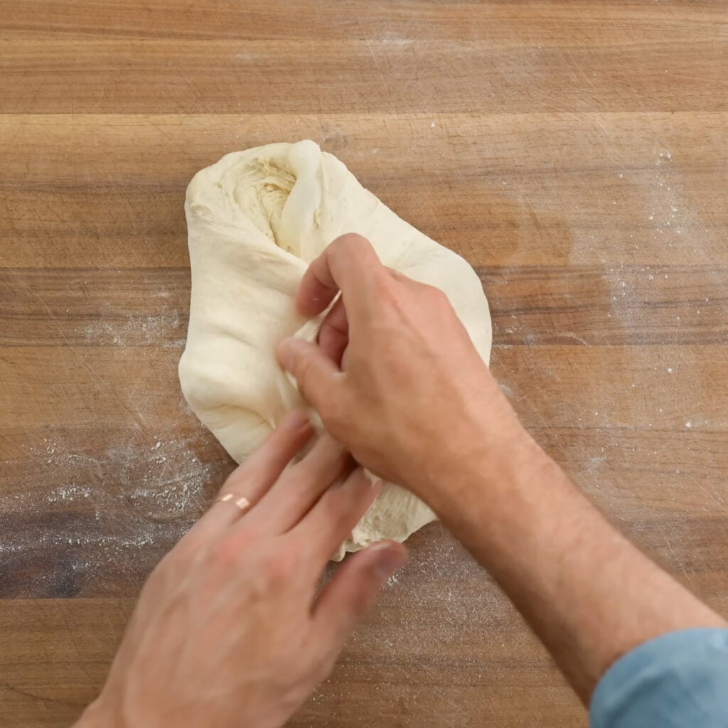 hands folding bread dough on wood cutting board