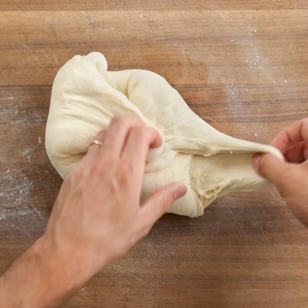 hands folding dough ball on wood cutting board
