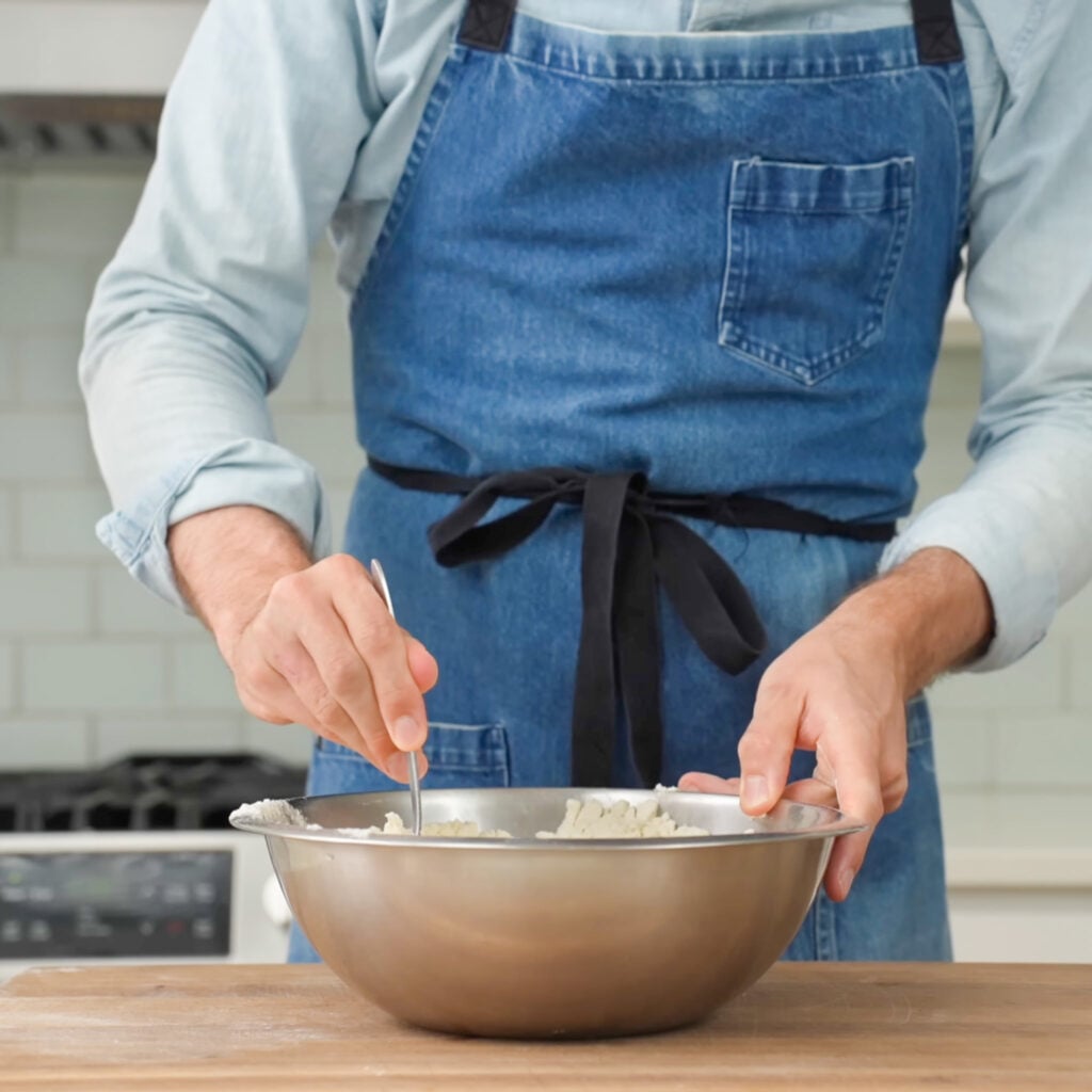 man in blue apron stirring dough in bowl with silver spoon