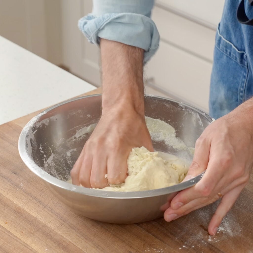 man squeezing dough in silver bowl