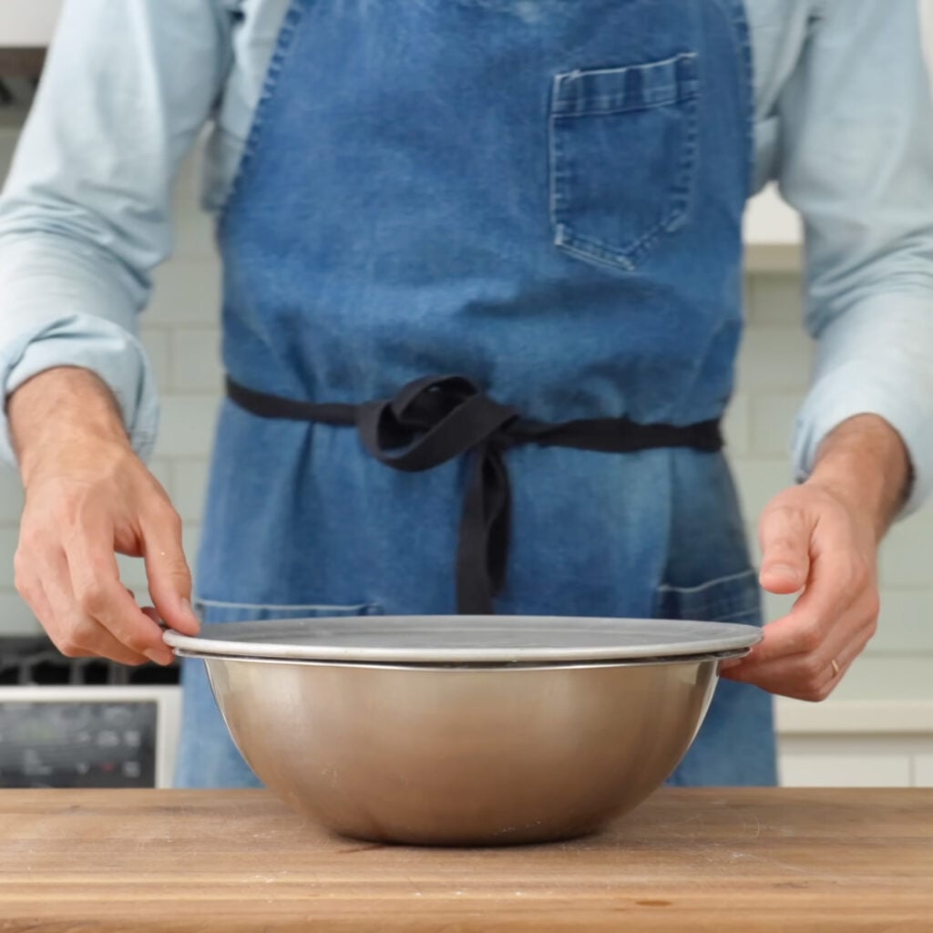 man in blue apron covering silver bowl with silver lid
