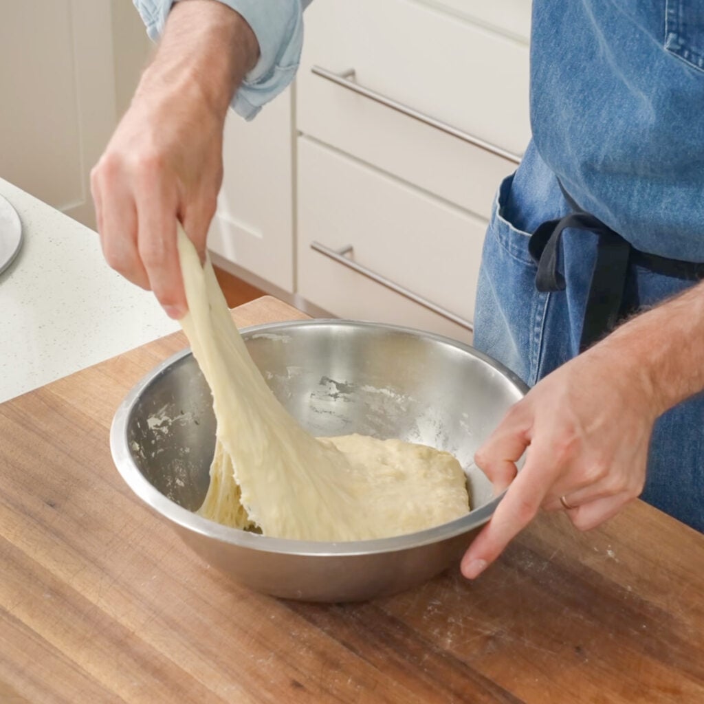 man stretching dough in silver bowl
