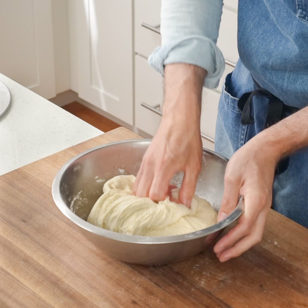 man kneading dough in silver bowl