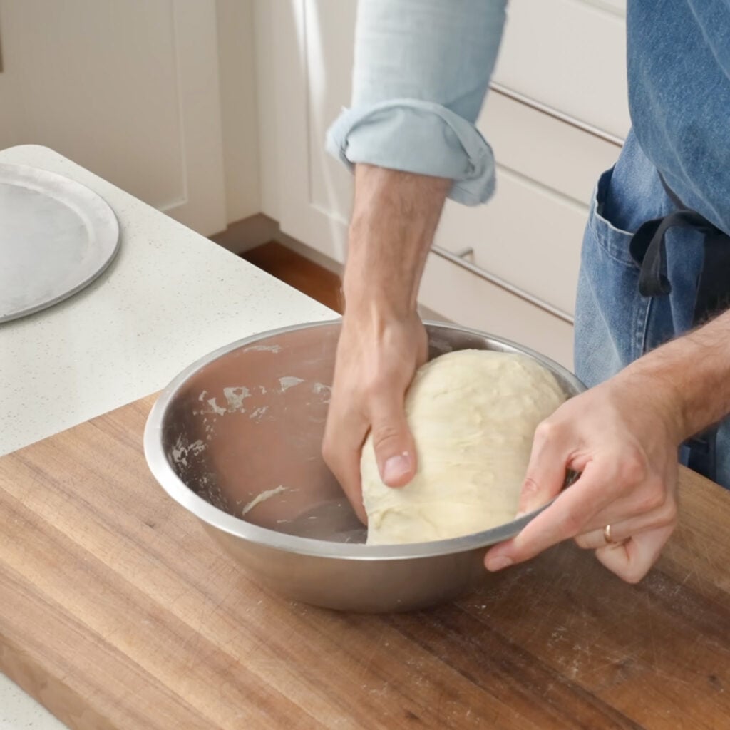 man rounding ball of dough in silver bowl