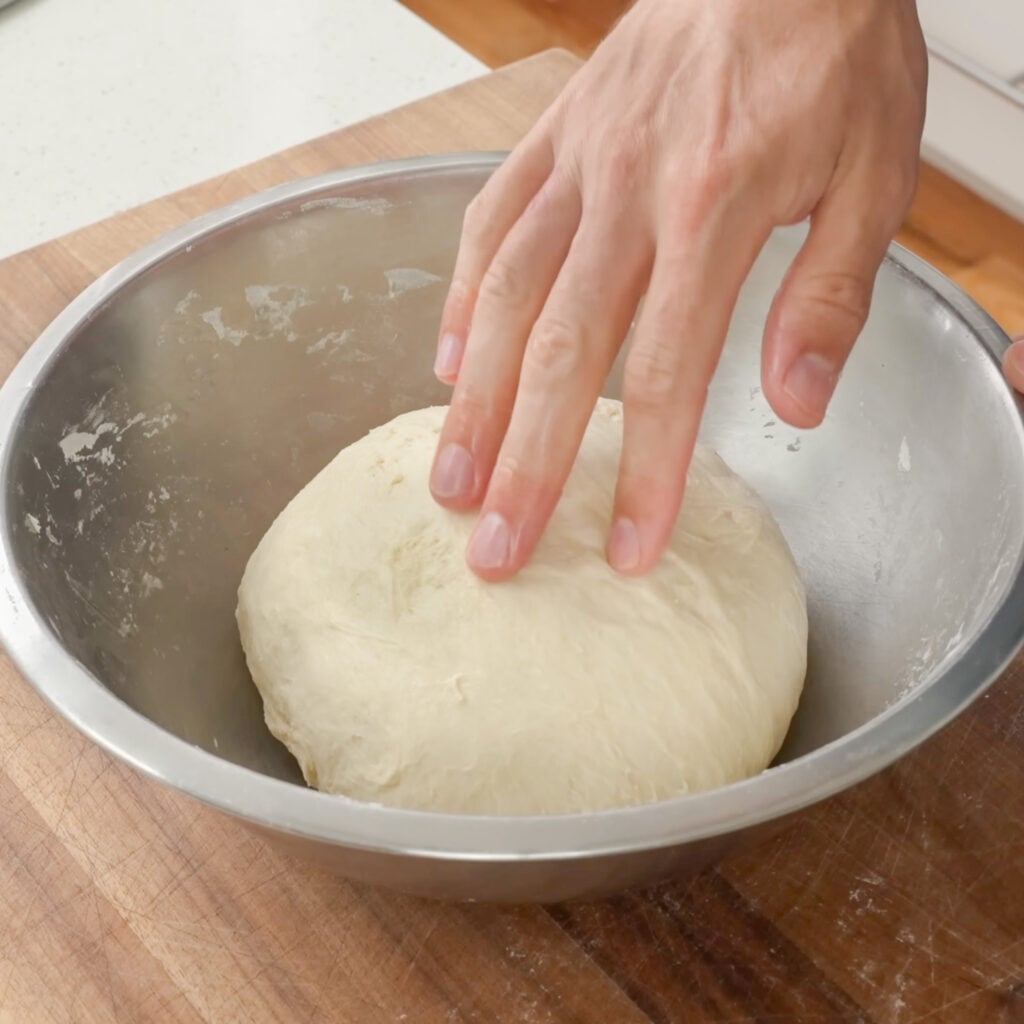 hand poking ball of dough in silver bowl