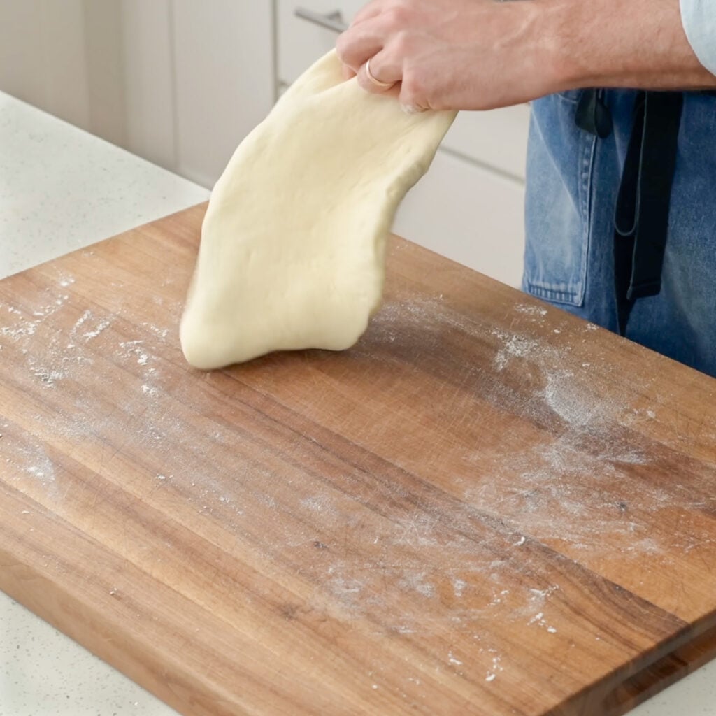 hand stretching pizza dough on wood cutting board
