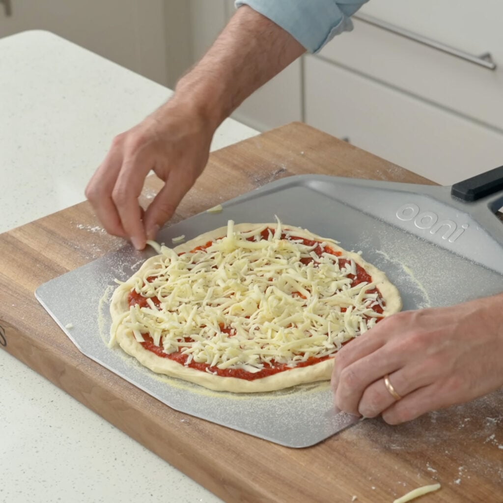 pizza dough with cheese and sauce on a pizza peel