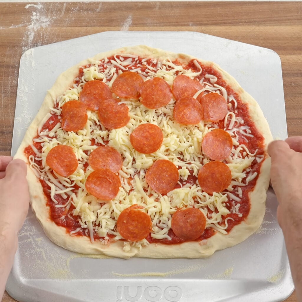stretching raw pepperoni pizza on pizza peel