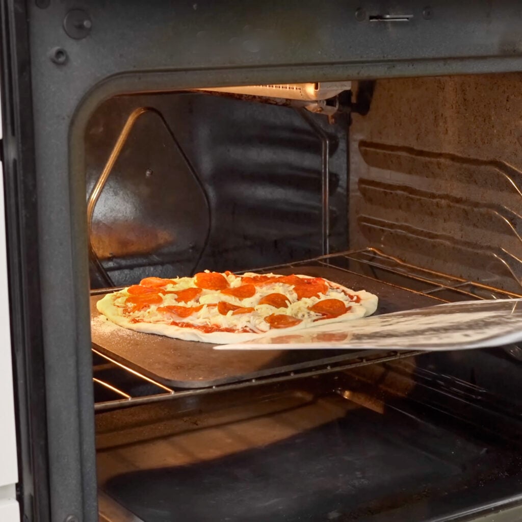 launching raw pizza onto pizza steel in oven