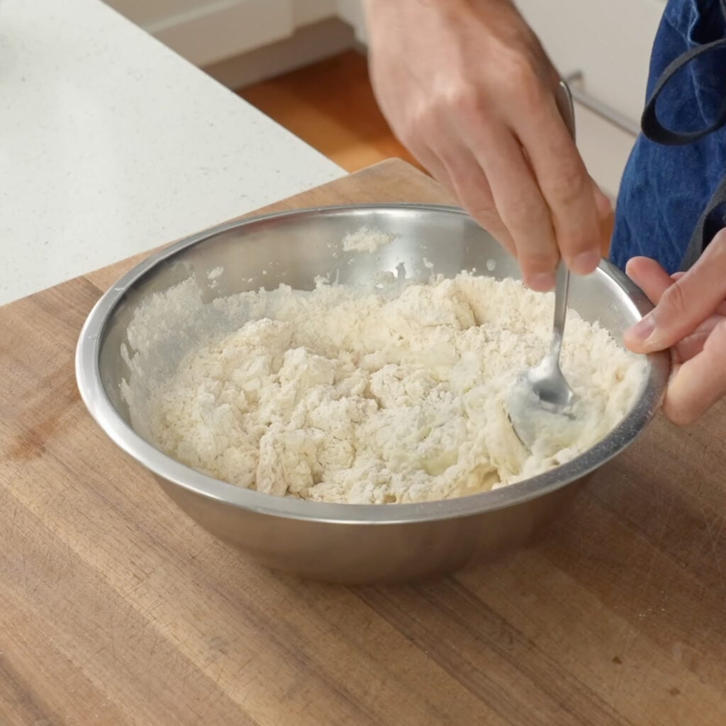 mixing dough with spoon in metal bowl