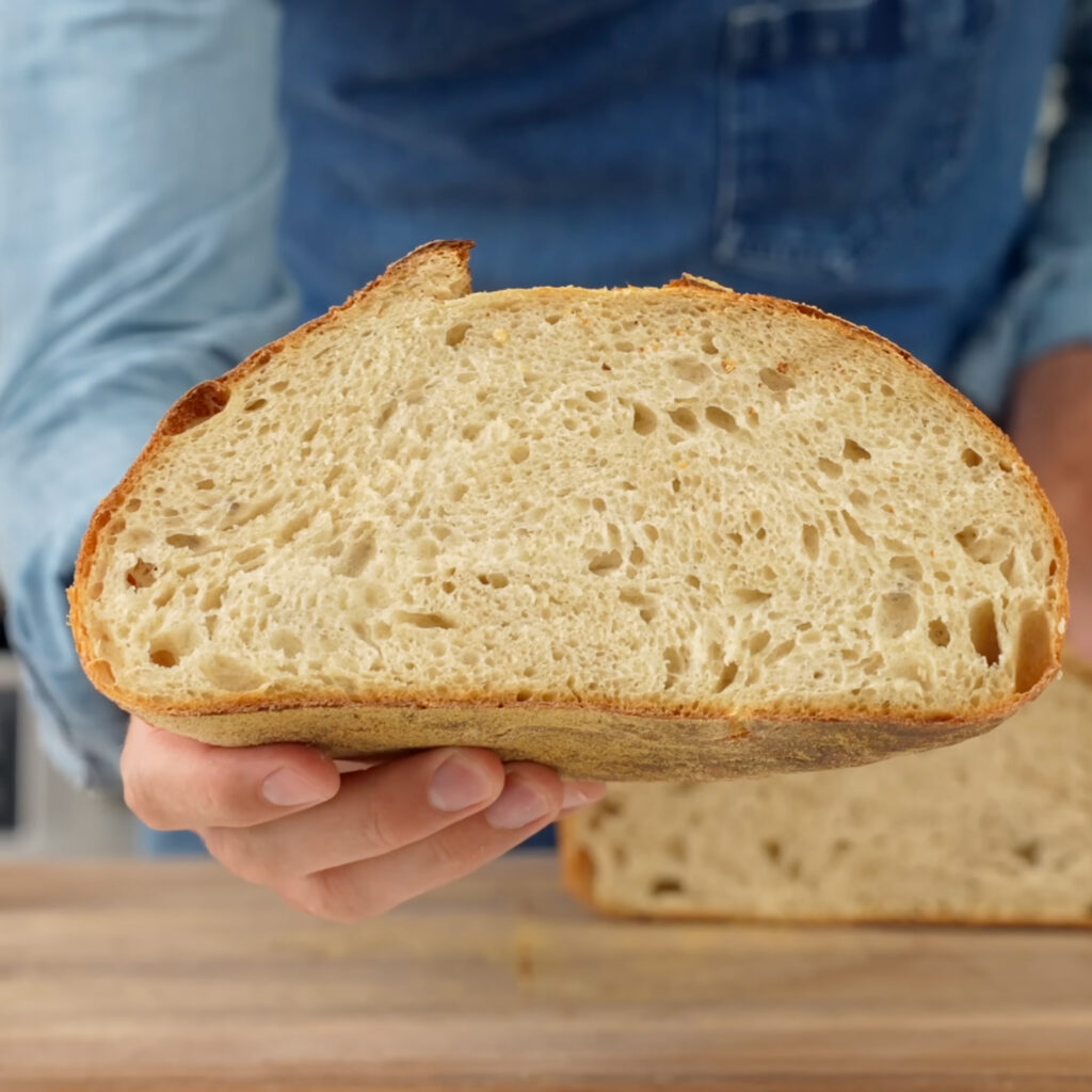 man in blue shirt holding up cross section of sourdough loaf