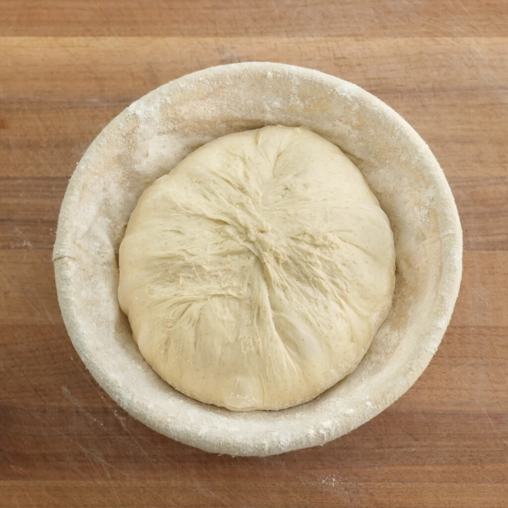 sourdough boule dough in proofing basket on wood cutting board