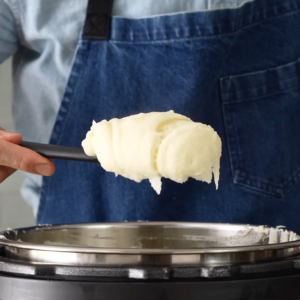 man holds black spoon of potato puree