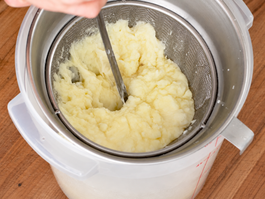 pushing mashed potatoes through fine mesh strainer with ladle