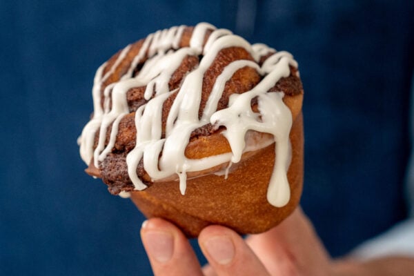 hand presenting cinnamon roll in front of blue background