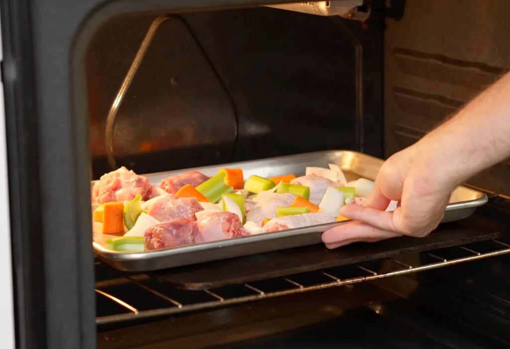 loading sheet pan into oven with cut turkey neck and wing pieces onion celery carrot