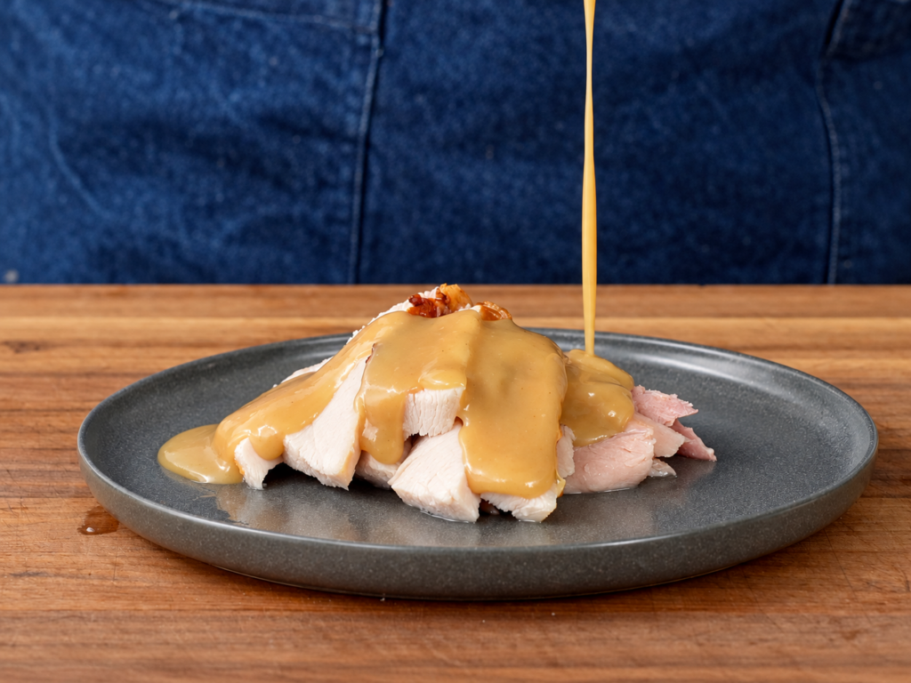 gravy dripping onto grey plate filled with slices of roast turkey