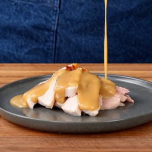 gravy dripping onto grey plate filled with slices of roast turkey