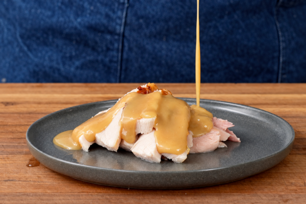 gravy dripping onto grey plate filled with slices of roast turkey