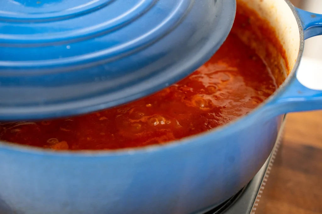 covered tomato sauce simmering in a blue dutch oven