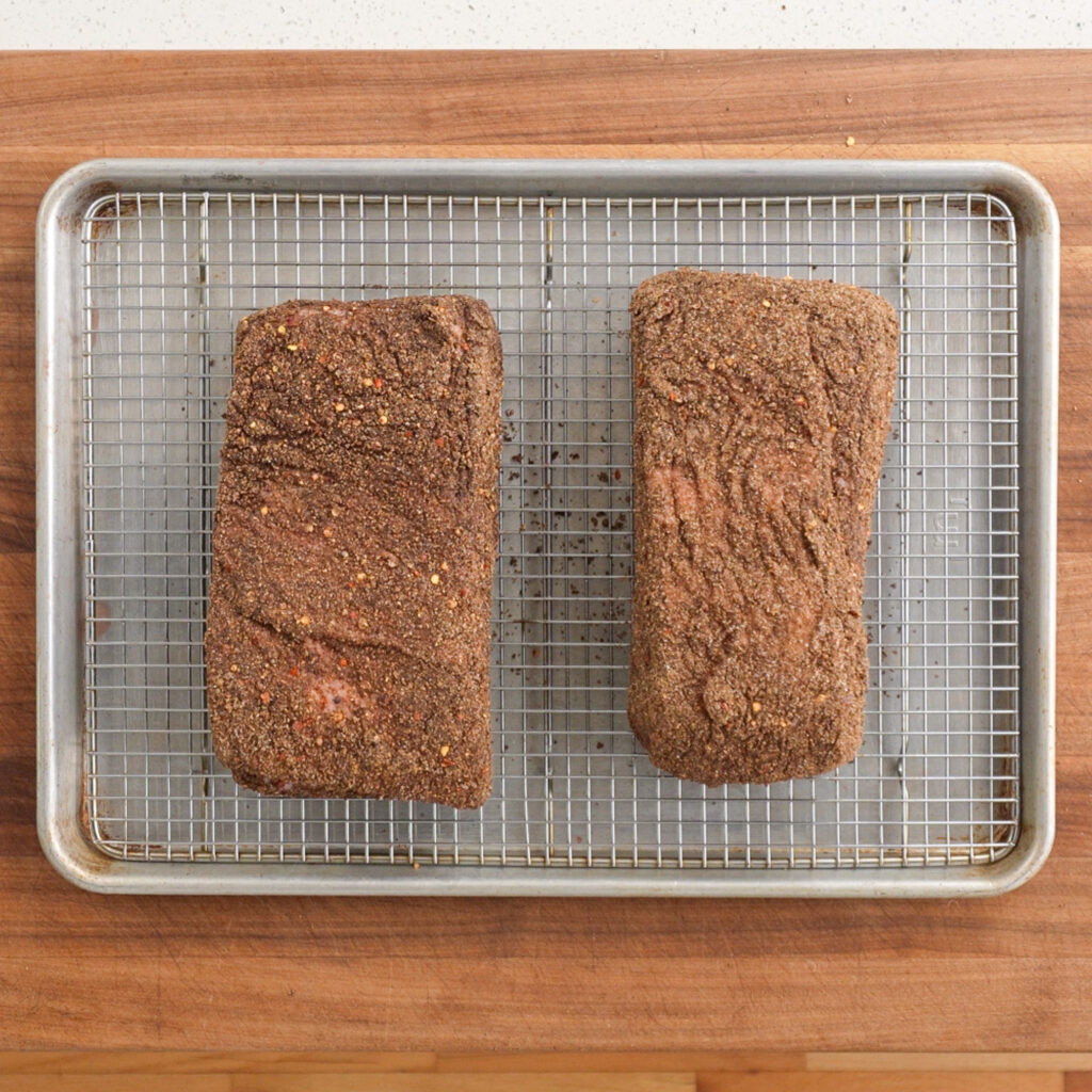 two pieces of rubbed corned beef on a sheet tray