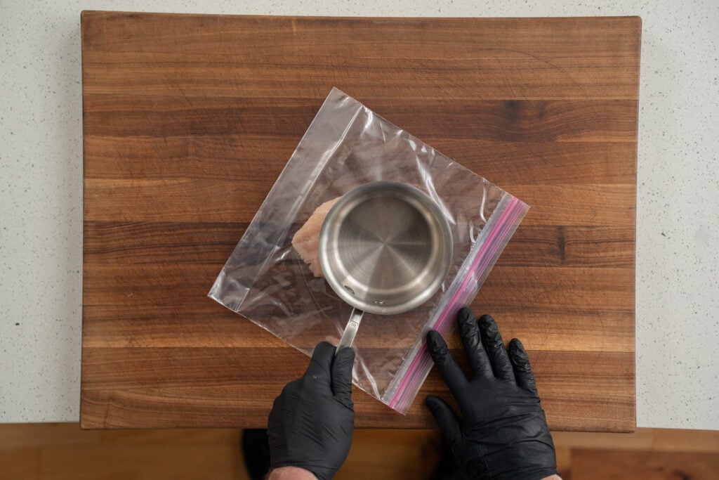 thinly pounding chicken breast in a storage bag with sauce pan