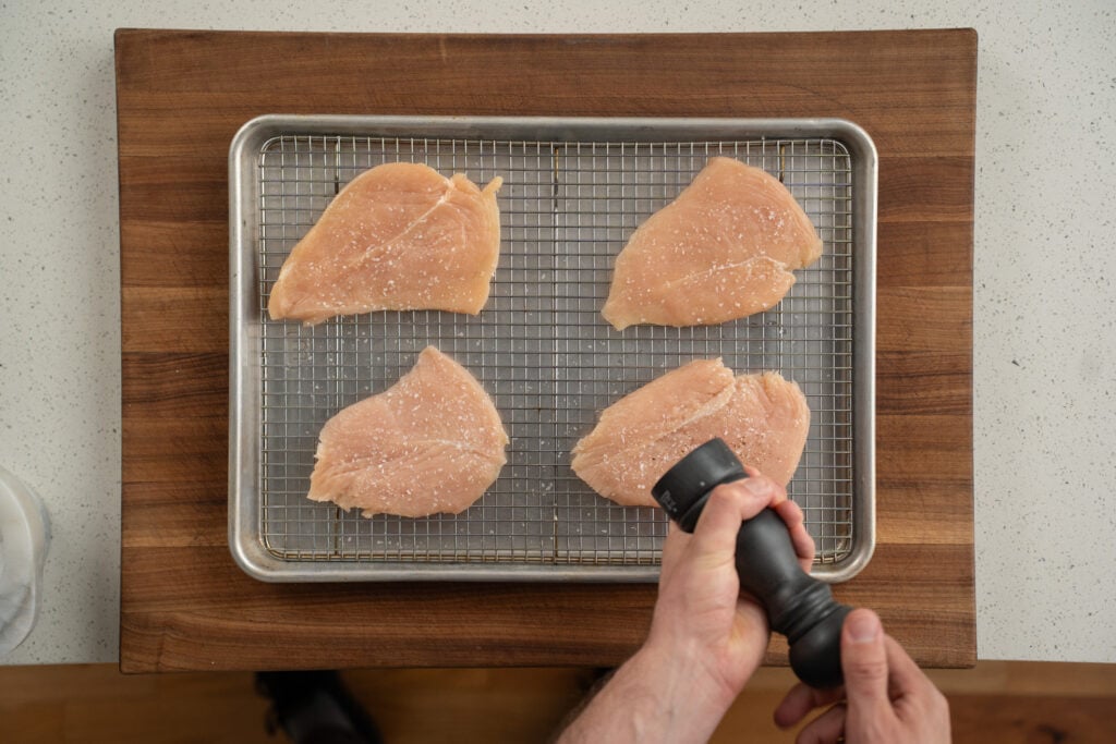 seasoning chicken breasts on wire rack with salt and pepper