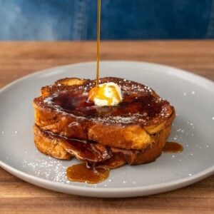 streaming maple syrup onto two pieces of French toast on grey plate