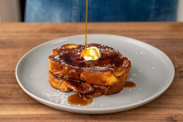 streaming maple syrup onto two pieces of French toast on grey plate