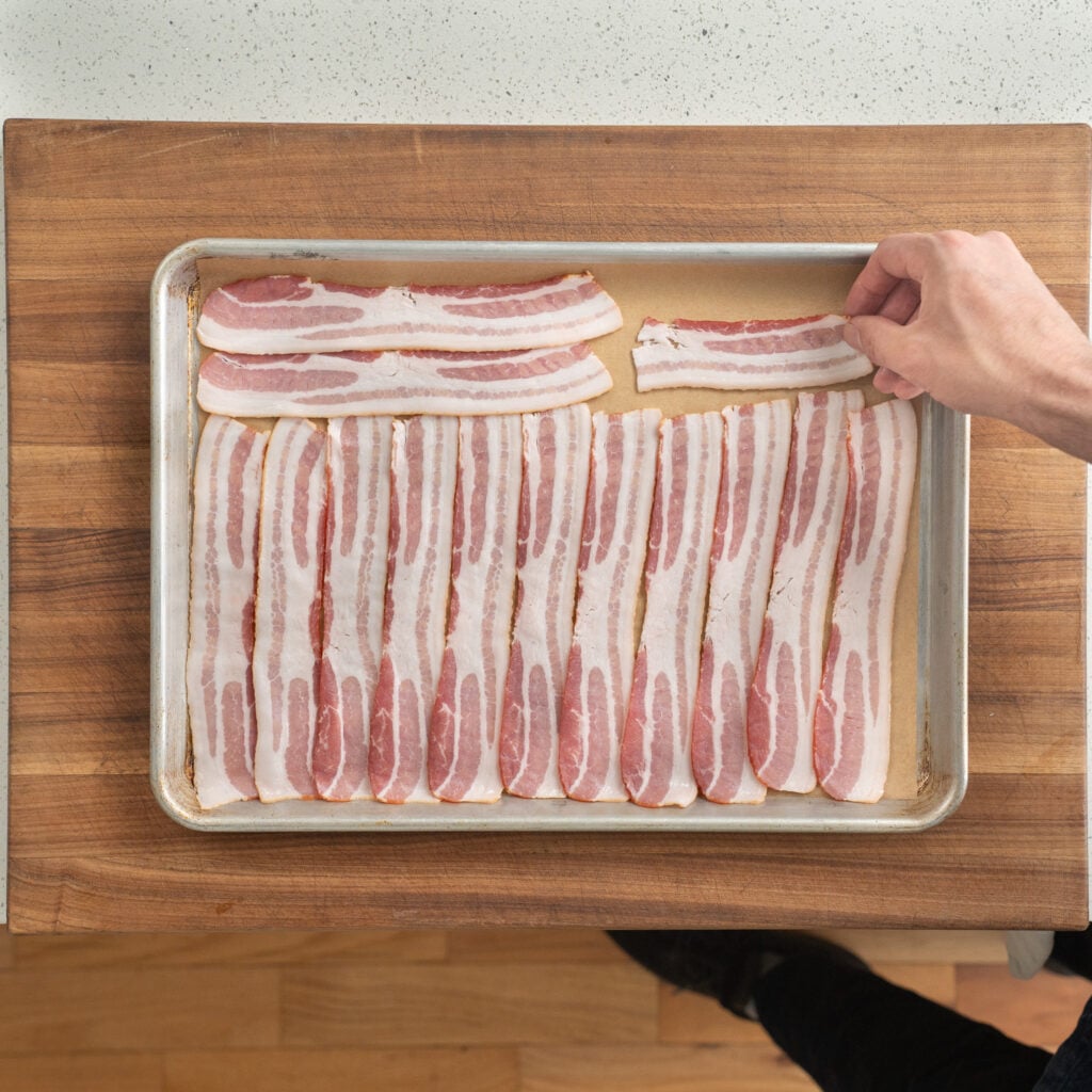 laying strips of bacon on a sheet tray 