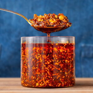 spoon full of chili crisp being lifted out of a glass container