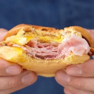 hands holding ham egg cheese sandwich with bite taken out