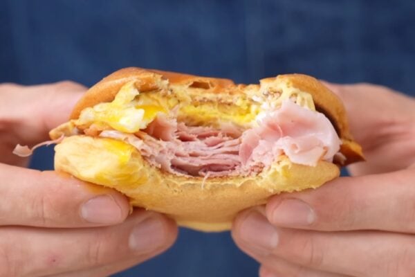 hands holding ham egg cheese sandwich with bite taken out