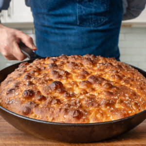 man holding black cast iron pan with baked golden brown focaccia
