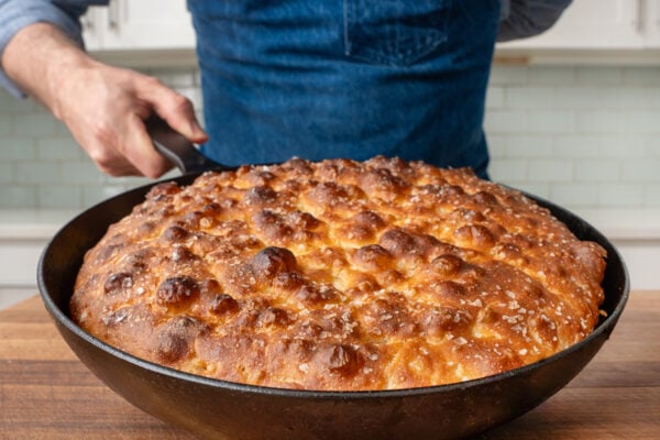man holding black cast iron pan with baked golden brown focaccia