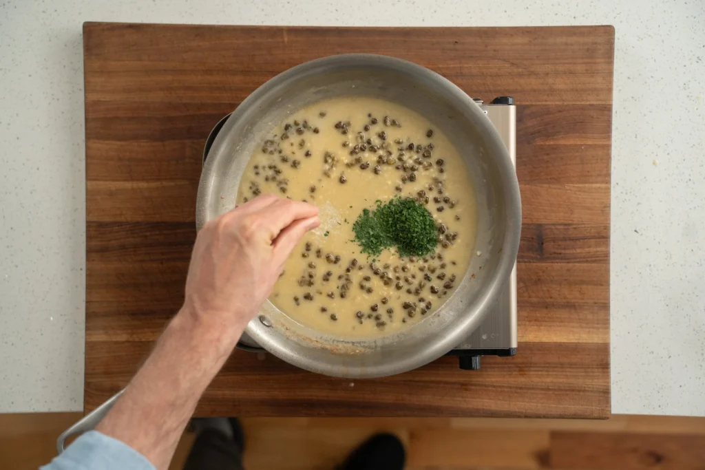 adding parsley to white wine caper butter sauce