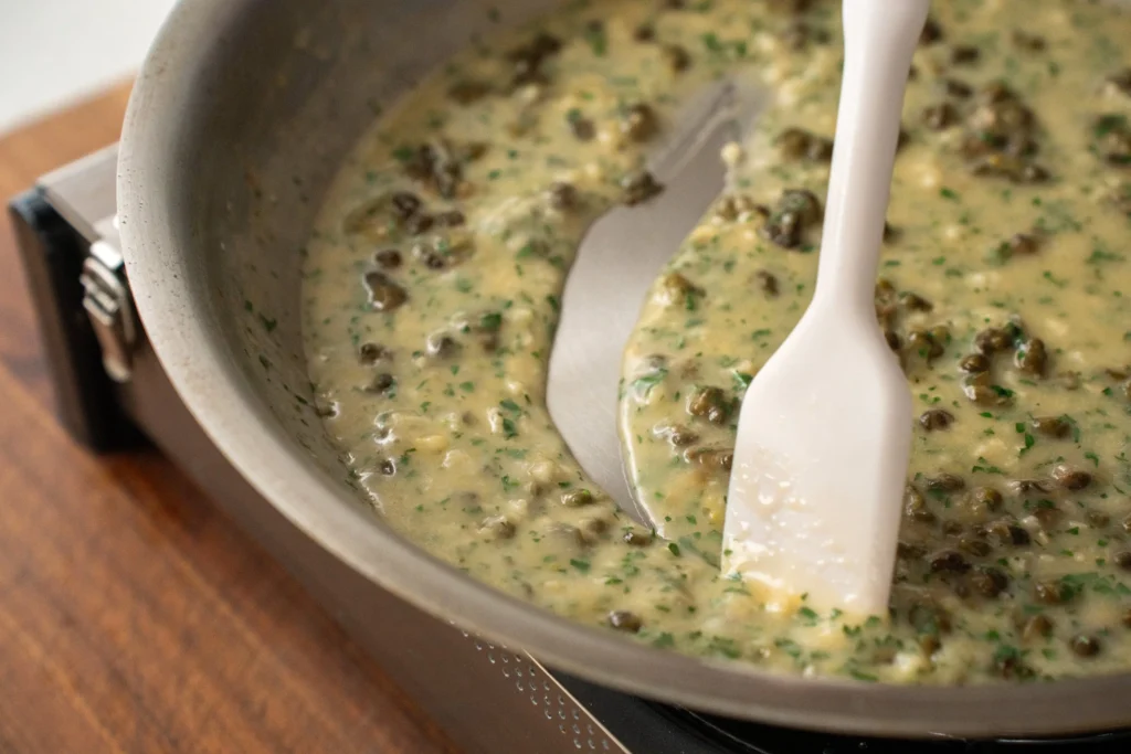 spatula leaving a trail through white wine caper butter sauce in a saute pan