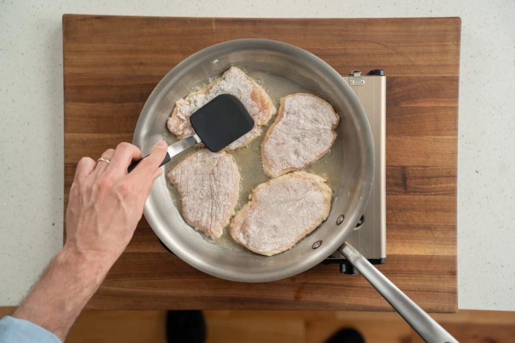 pressing breaded chicken breast with spatula in a saute pan