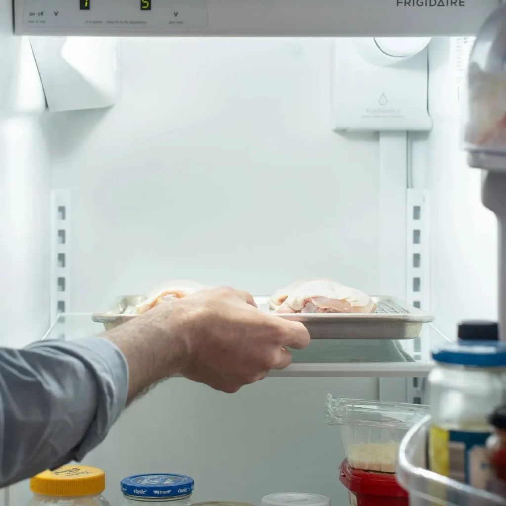 placing sheet tray of chicken thighs in refrigerator