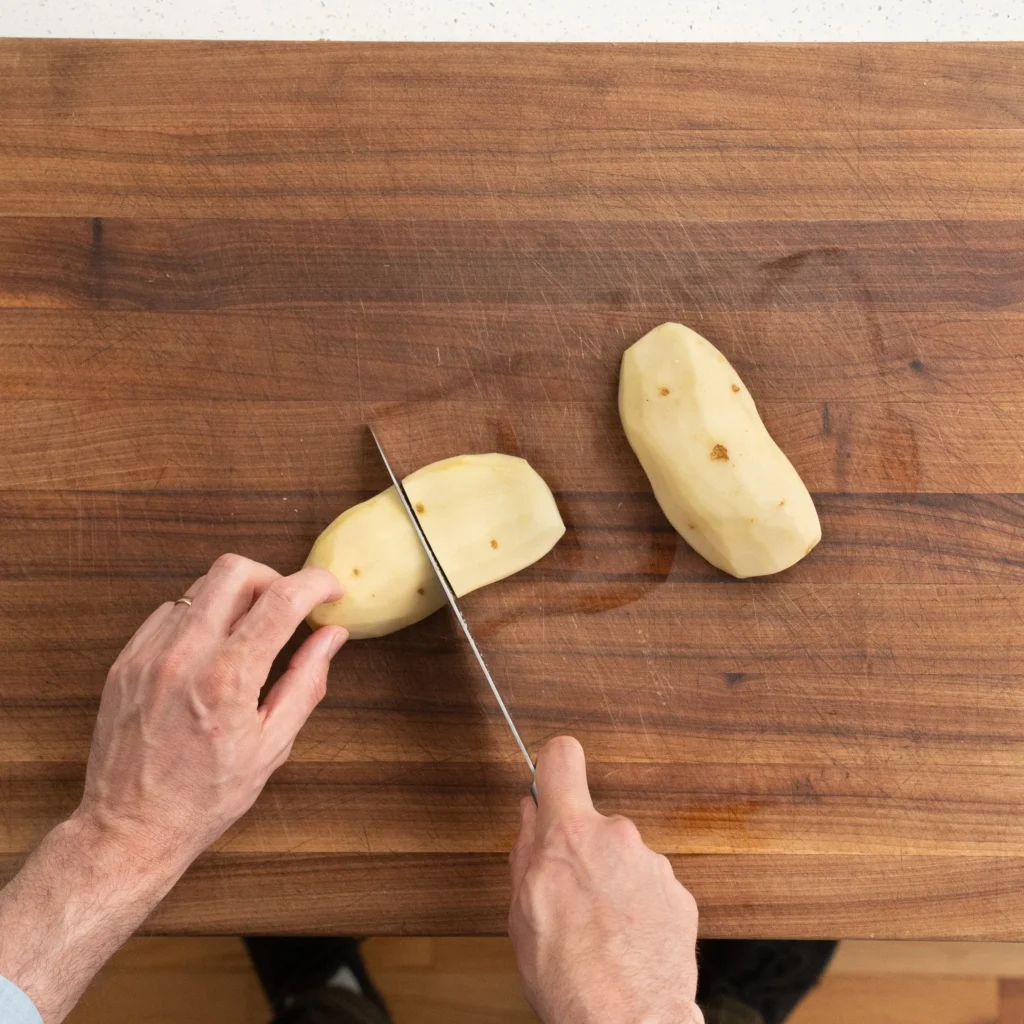 cutting potato on wooden cutting board with chefs knife
