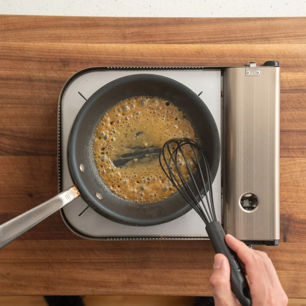 whisking bubbling gravy in saute pan with black whisk