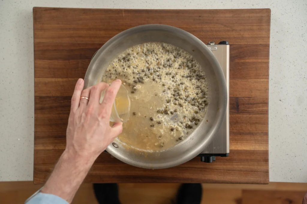 adding stock to capers and garlic in a saute pan