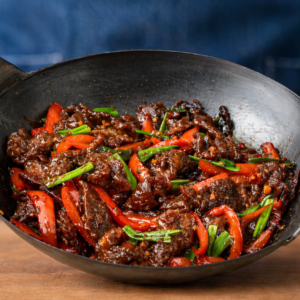 Mongolian beef in a wok on a wooden cutting board