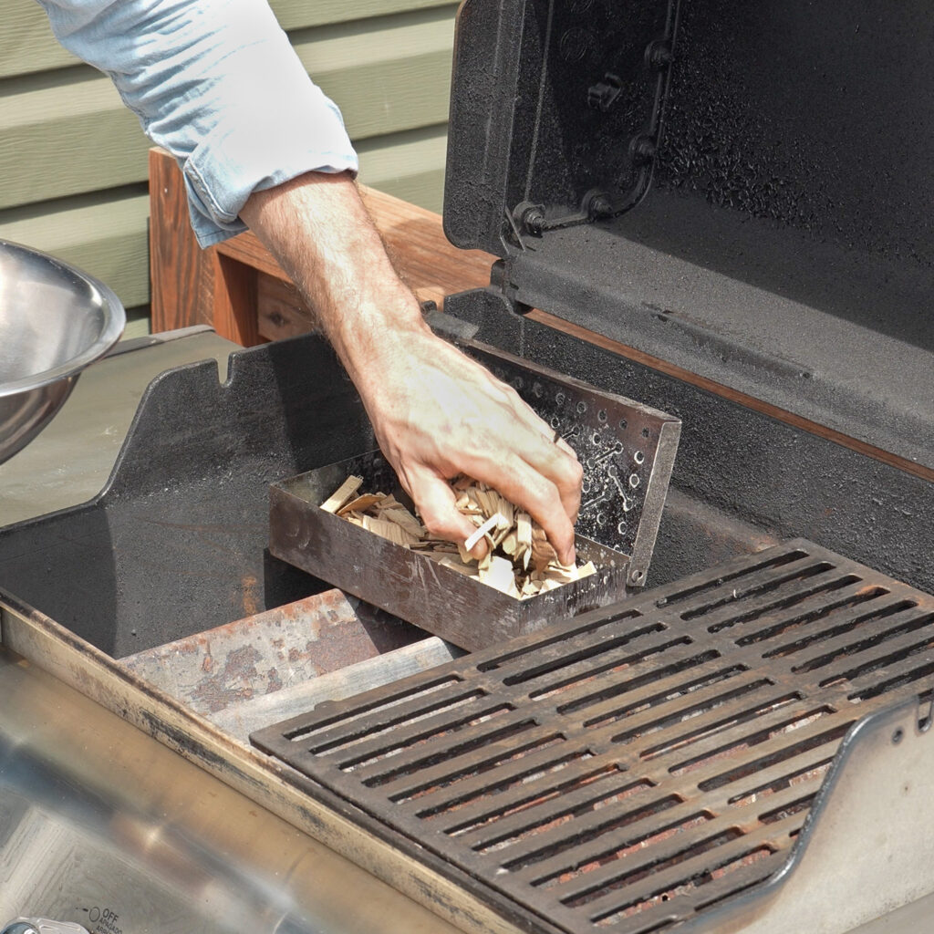 adding wood chips to smoker box on a grill